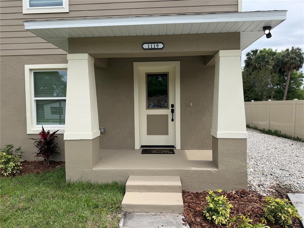 A tan house exterior features a covered front porch with two white tapered columns — 1119 WILLOW AVENUE, SANFORD, FL