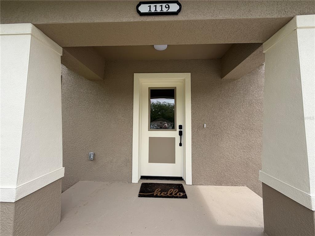 A covered entryway features a beige front door with a window and a welcome mat — 1119 WILLOW AVENUE, SANFORD, FL