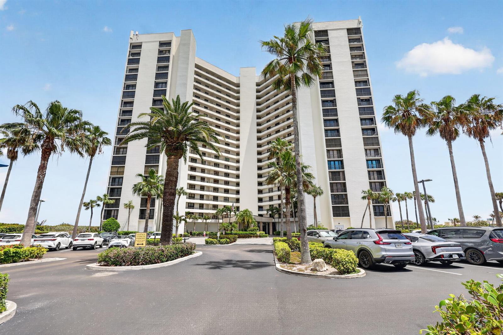 A tall, white residential high-rise building stands behind a parking lot with palm trees — 9650 S Ocean Drive # 507, Jensen Beach FL 34957, JENSEN BEACH, FL