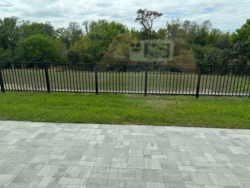 A paved patio overlooks a grassy backyard enclosed by a black metal fence — 7920 SPECTRUM DRIVE, KISSIMMEE, FL