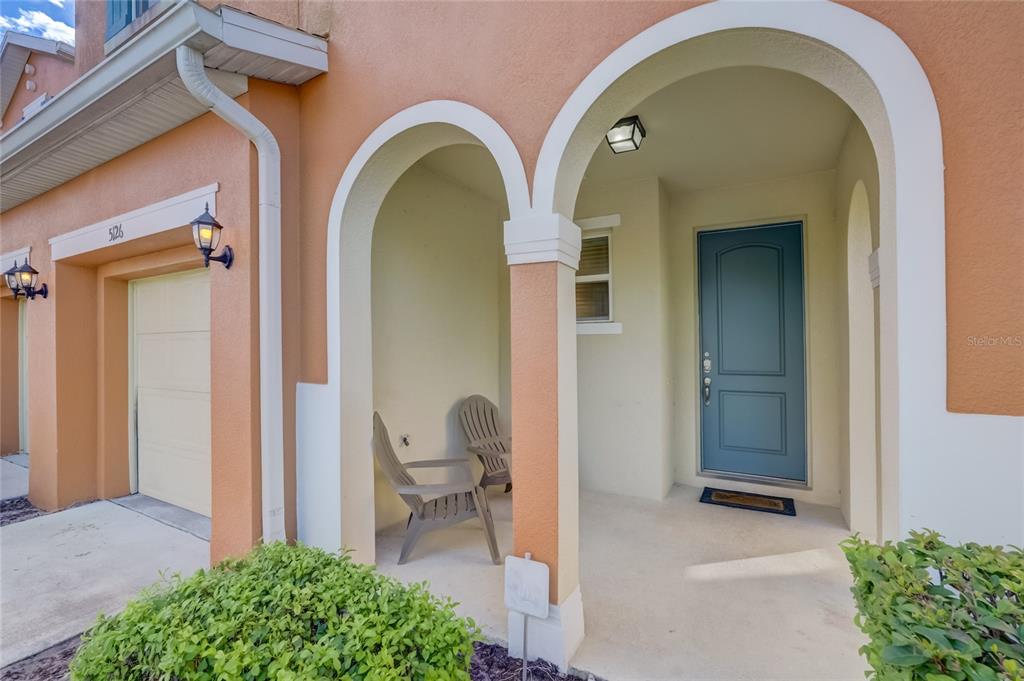 The exterior of a home features a covered entryway with two arched openings and chairs — 5126 ADELAIDE DRIVE, KISSIMMEE, FL