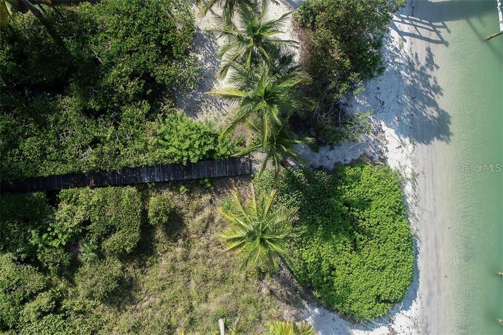 An aerial view shows a wooden boardwalk winding through lush vegetation and palm trees near water — 16080 GULF SHORES DRIVE, BOCA GRANDE, FL