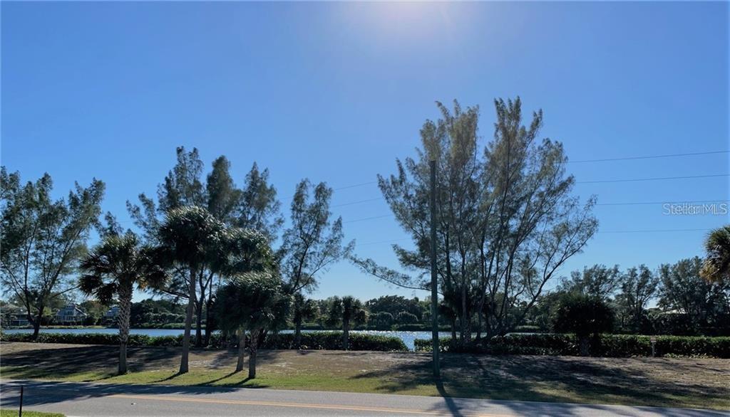 A view of a grassy lot with trees and a body of water in the background — 16080 GULF SHORES DRIVE, BOCA GRANDE, FL