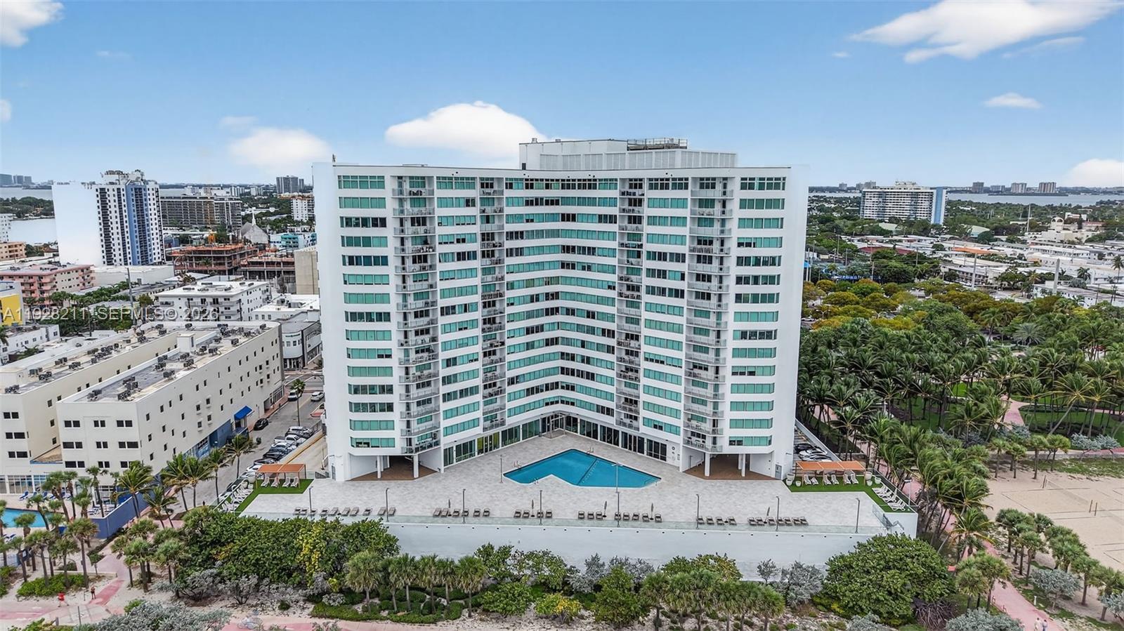An aerial view shows a tall, curved residential building with a swimming pool and patio — 7135 Collins Ave # 1015, Miami Beach FL 33141, MIAMI BEACH, FL