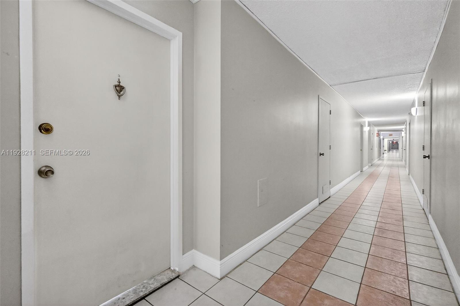 A long, narrow apartment hallway features white doors, light gray walls, and tiled flooring — 7135 Collins Ave # 1015, Miami Beach FL 33141, MIAMI BEACH, FL