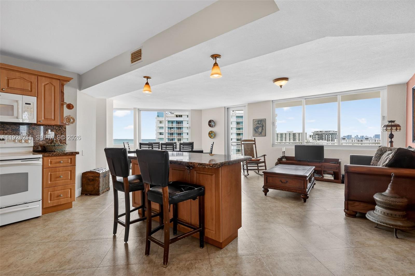 An open-concept kitchen and living area features wood cabinetry, a granite island, and ocean views — 7135 Collins Ave # 1015, Miami Beach FL 33141, MIAMI BEACH, FL
