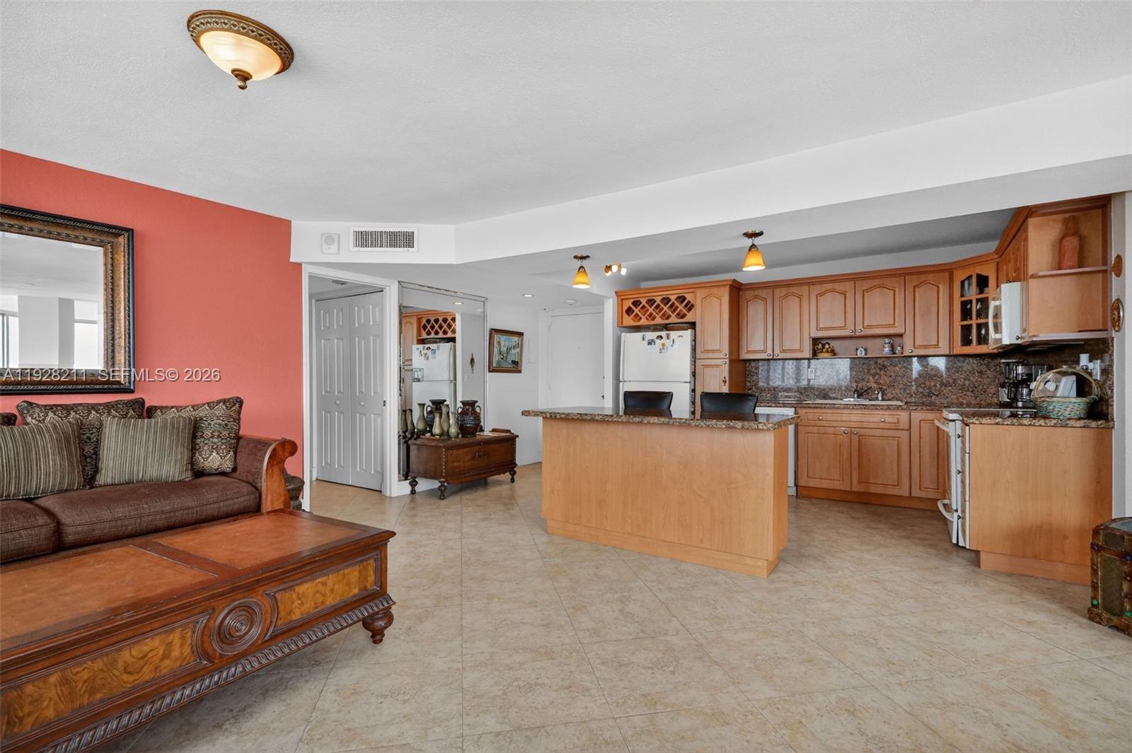 An open-concept living room and kitchen featuring tile floors, wood cabinetry, and a breakfast bar — 7135 Collins Ave # 1015, Miami Beach FL 33141, MIAMI BEACH, FL