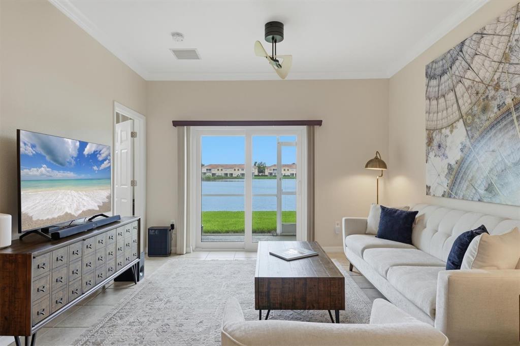 A living room features a sofa, coffee table, television, and sliding doors overlooking a lake — 3582 PARKRIDGE CIRCLE UNIT 29-106, SARASOTA, FL