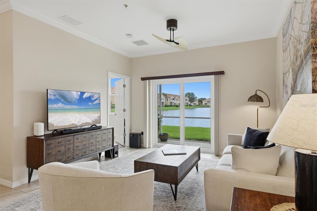 A living room with a television, sofa, coffee table, and sliding glass doors overlooking a lake — 3582 PARKRIDGE CIRCLE UNIT 29-106, SARASOTA, FL
