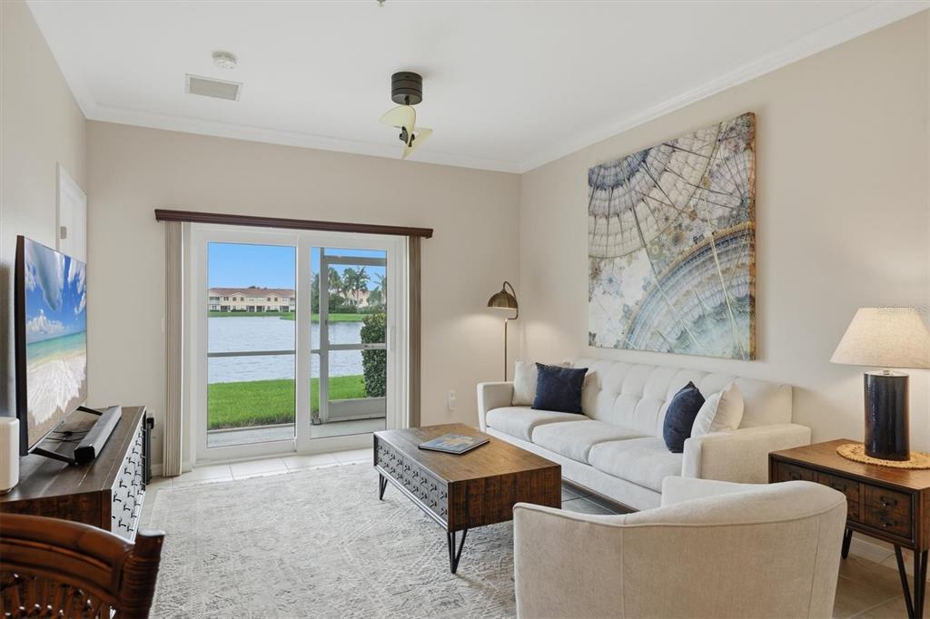 A living room features a white sofa, coffee table, and sliding doors overlooking a lake — 3582 PARKRIDGE CIRCLE UNIT 29-106, SARASOTA, FL