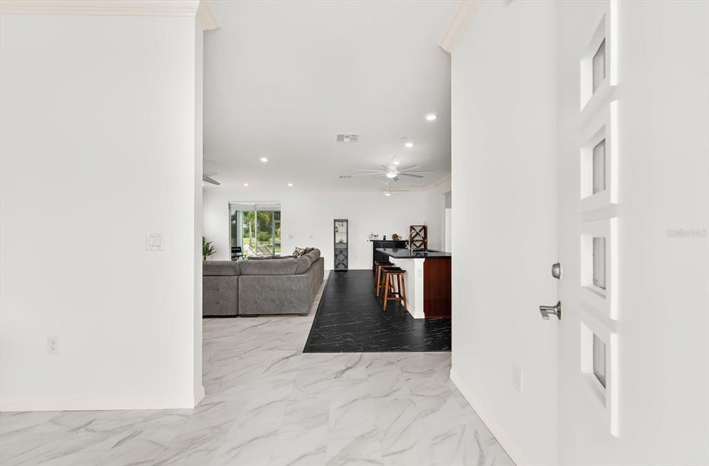 A view from an entryway into an open-concept living area with marble-look and dark flooring — 2365 MAURITANIA ROAD, PUNTA GORDA, FL