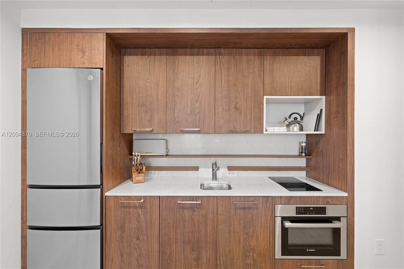 A modern kitchenette features wood-grain cabinetry, stainless steel appliances, and a white stone countertop — 1611 SW 2nd Ave # 816, Miami FL 33129, MIAMI, FL
