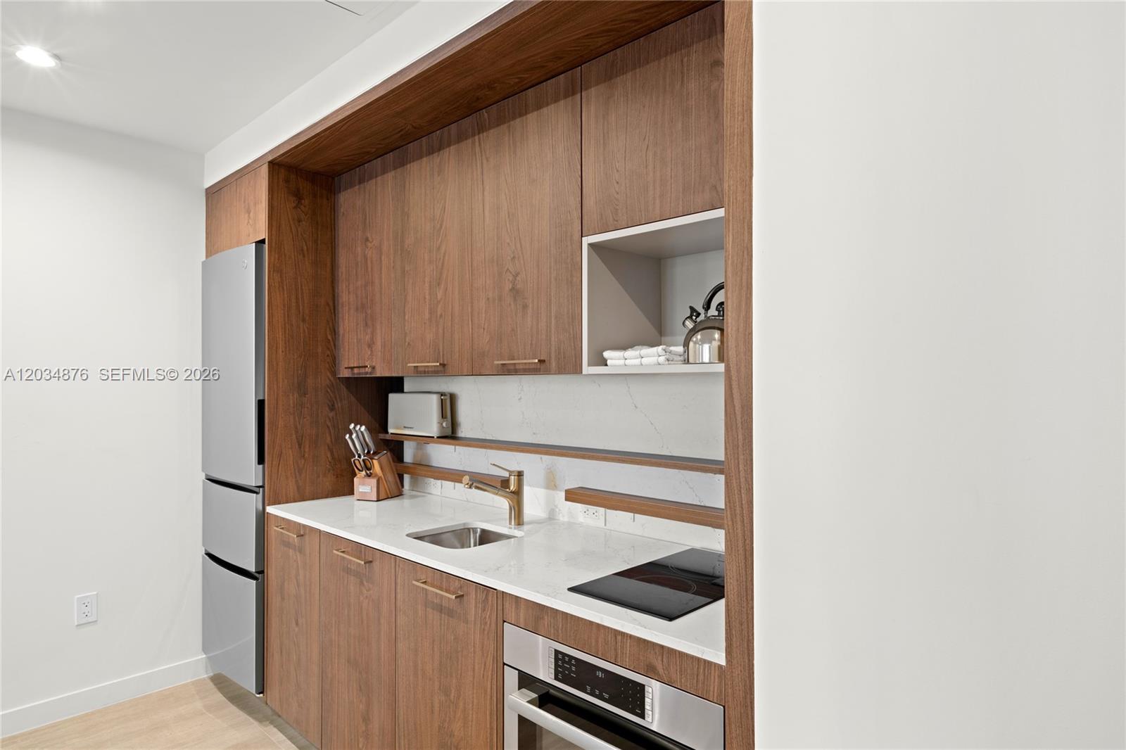 A modern kitchenette features wood cabinetry, a white countertop, a stainless steel refrigerator, and appliances — 1611 SW 2nd Ave # 816, Miami FL 33129, MIAMI, FL