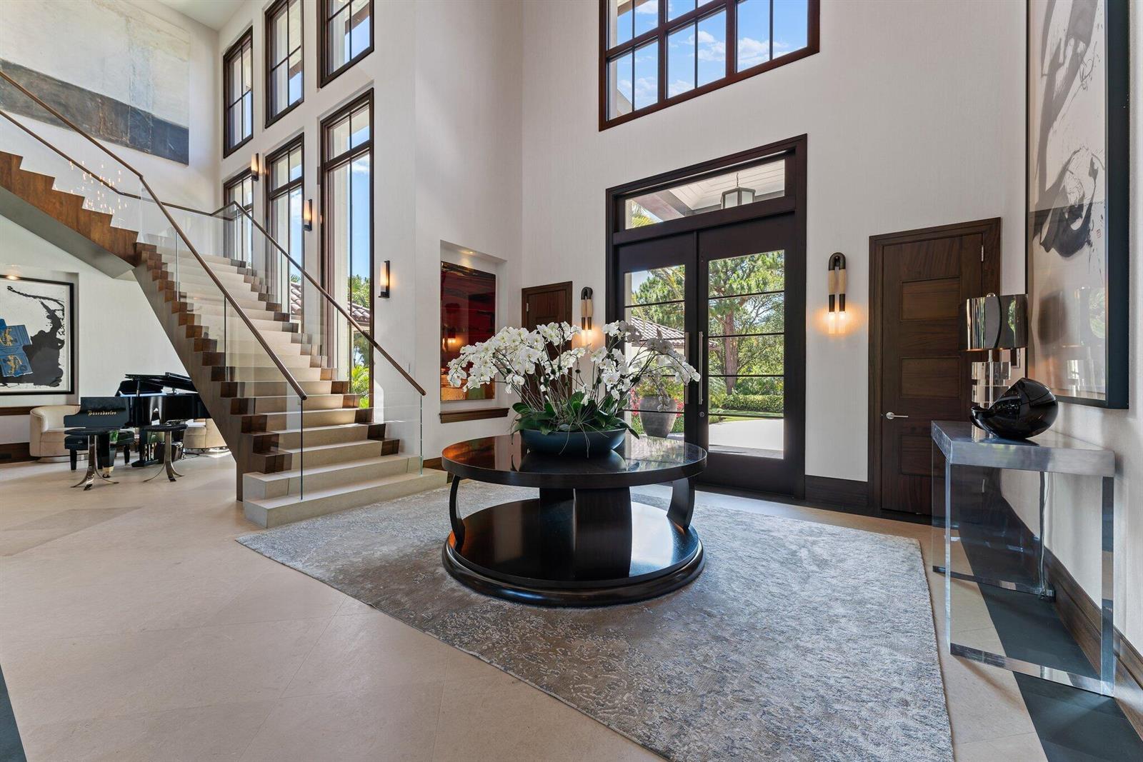 A grand foyer features a floating staircase, a central circular table, and double glass doors — 232 Bears Club Drive, Jupiter FL 33477, JUPITER, FL