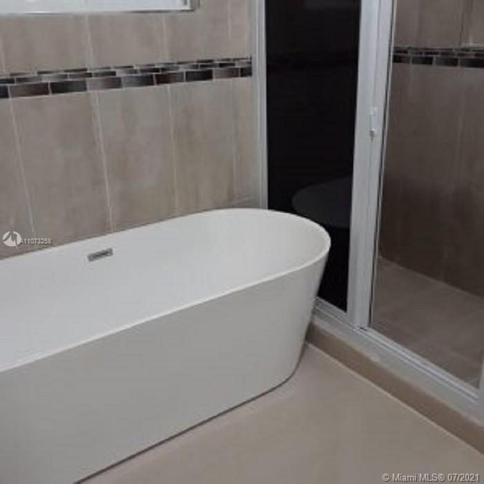 A modern white freestanding bathtub sits next to a glass-enclosed shower in a tiled bathroom — 1 Sanctuary At Farm Hill Jamaic, JM JMCAN19, JM