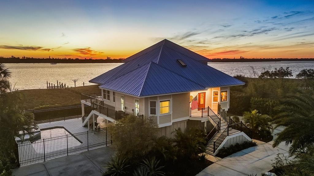 An elevated house with a blue metal roof sits beside a pool and water — 9941 EAGLE PRESERVE DRIVE, ENGLEWOOD, FL