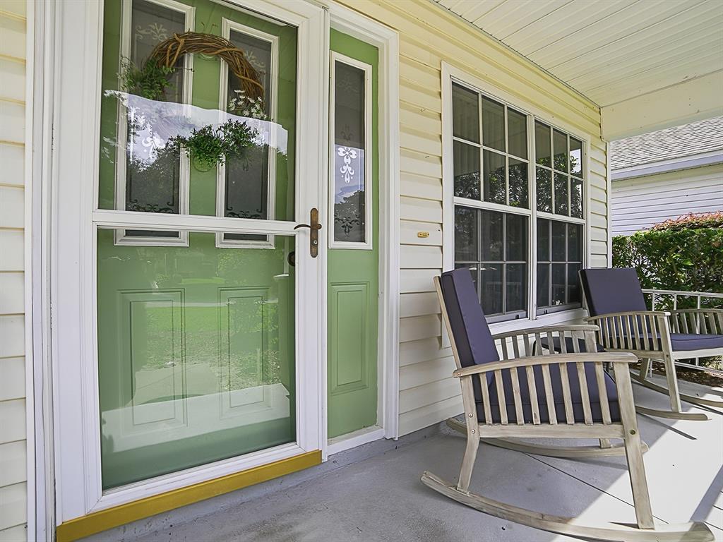A front porch features a green door with a wreath, siding, and two wooden rocking chairs — 25114 CRANES ROOST CIRCLE, LEESBURG, FL