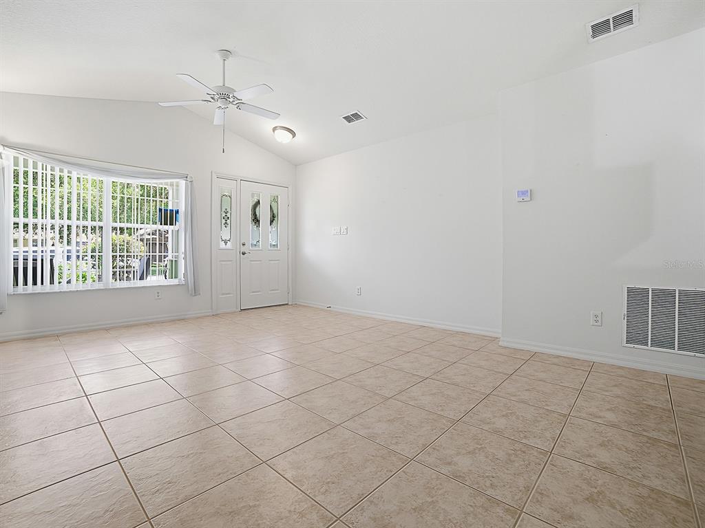 A bright living room features white walls, tan tile flooring, a ceiling fan, and windows — 25114 CRANES ROOST CIRCLE, LEESBURG, FL