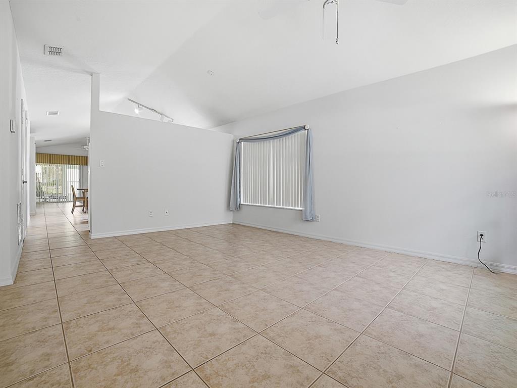 An empty living room features white walls, vaulted ceilings, and light-colored square floor tiles — 25114 CRANES ROOST CIRCLE, LEESBURG, FL