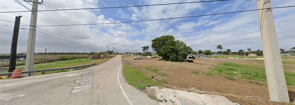 A paved road curves past a large, mostly vacant grassy lot with scattered trees and utility poles — RARDIN AVENUE, PAHOKEE, FL