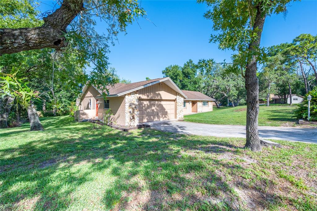 A tan, single-story house with a stone-accented garage and a large, tree-filled front yard — 800 SWEETWATER CREEK COURT, LONGWOOD, FL