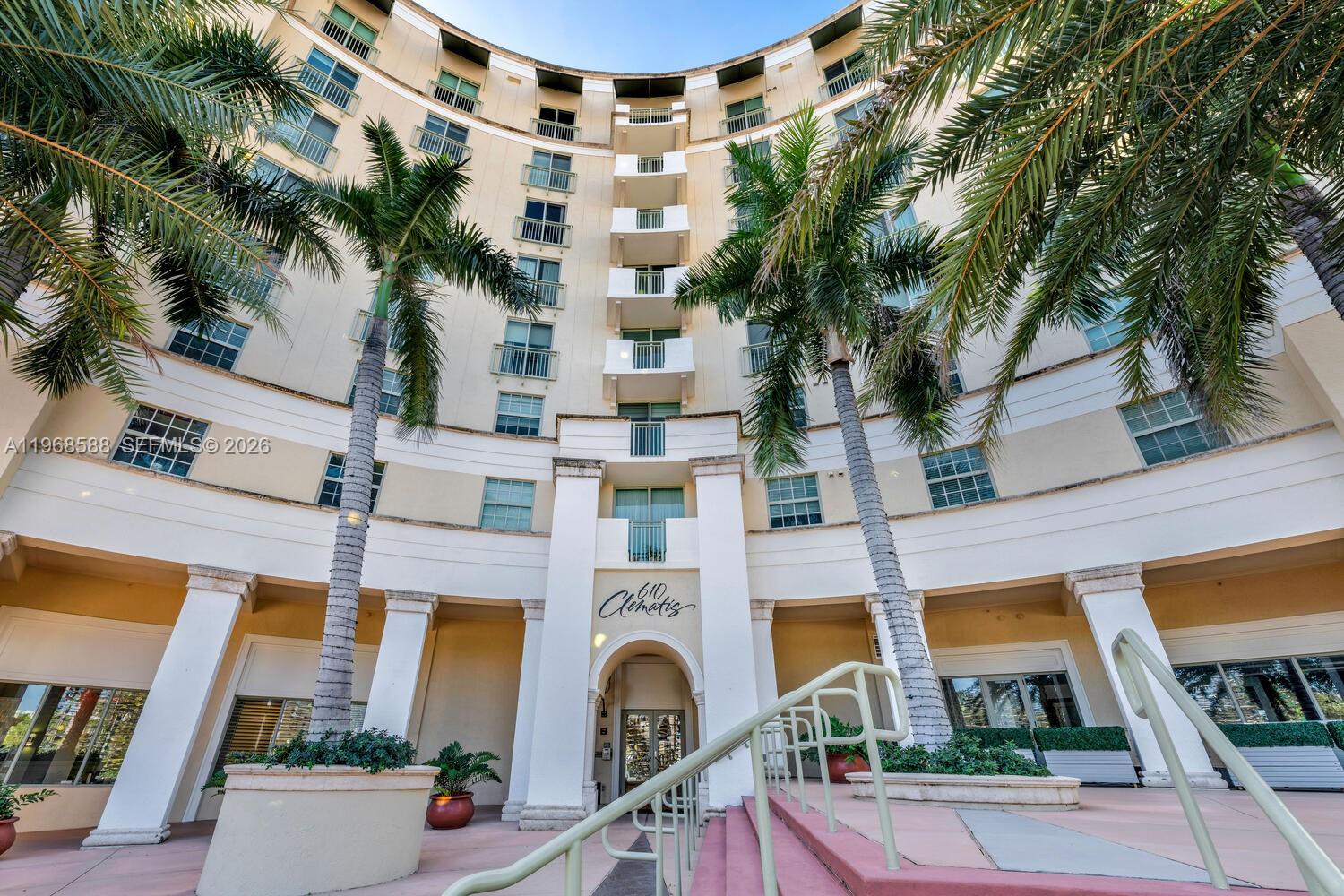 A low-angle view of a multi-story curved apartment building with palm trees and stairs — 610 Clematis St # 406, West Palm Beach FL 33401, WEST PALM BEACH, FL