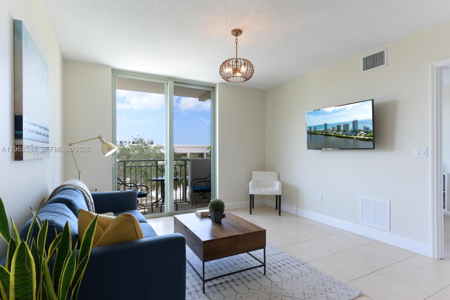 A living room features a blue sofa, a wooden coffee table, and a balcony view — 610 Clematis St # 406, West Palm Beach FL 33401, WEST PALM BEACH, FL