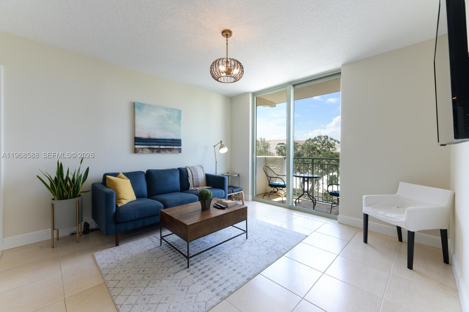 A living room features a blue sofa, a wooden coffee table, and a balcony view — 610 Clematis St # 406, West Palm Beach FL 33401, WEST PALM BEACH, FL