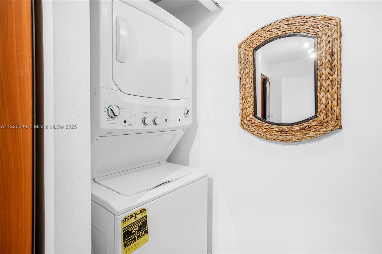 A laundry closet features a stacked washer and dryer unit next to a woven-framed mirror — 2080 S Ocean Dr,, Hallandale Beach FL 33009, HALLANDALE BEACH, FL