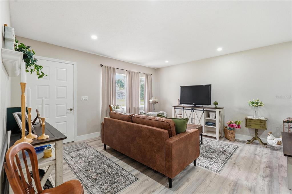A living room features light wood-look flooring, a brown sofa, and a television on a console — 11094 SW 79TH AVENUE, OCALA, FL