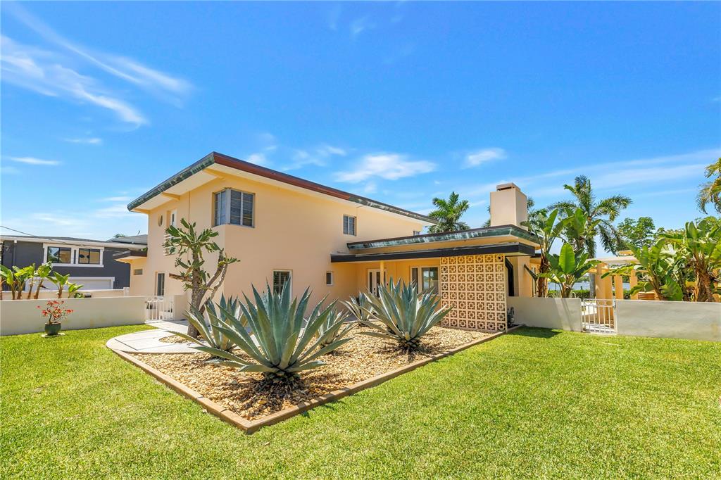 A two-story yellow house features a decorative breeze block wall and a landscaped gravel bed — 2781 BAYSIDE DRIVE S, ST PETERSBURG, FL