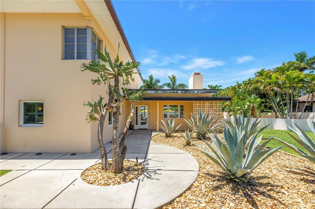 A beige house exterior features a concrete walkway, desert landscaping, and a decorative breeze block wall — 2781 BAYSIDE DRIVE S, ST PETERSBURG, FL