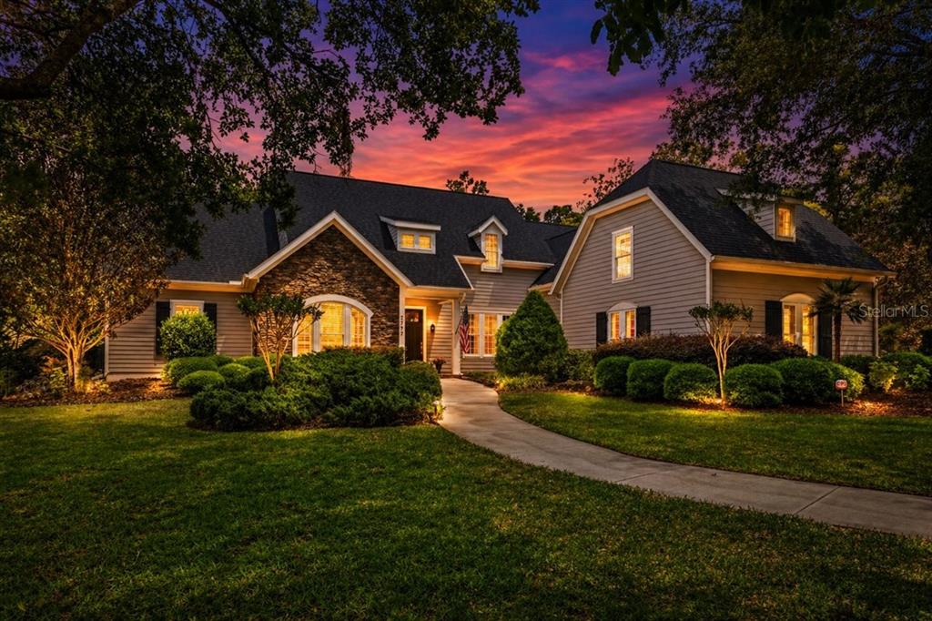 A two-story house with gray siding and stone accents sits behind a landscaped front yard — 2772 NW 26TH PLACE, GAINESVILLE, FL
