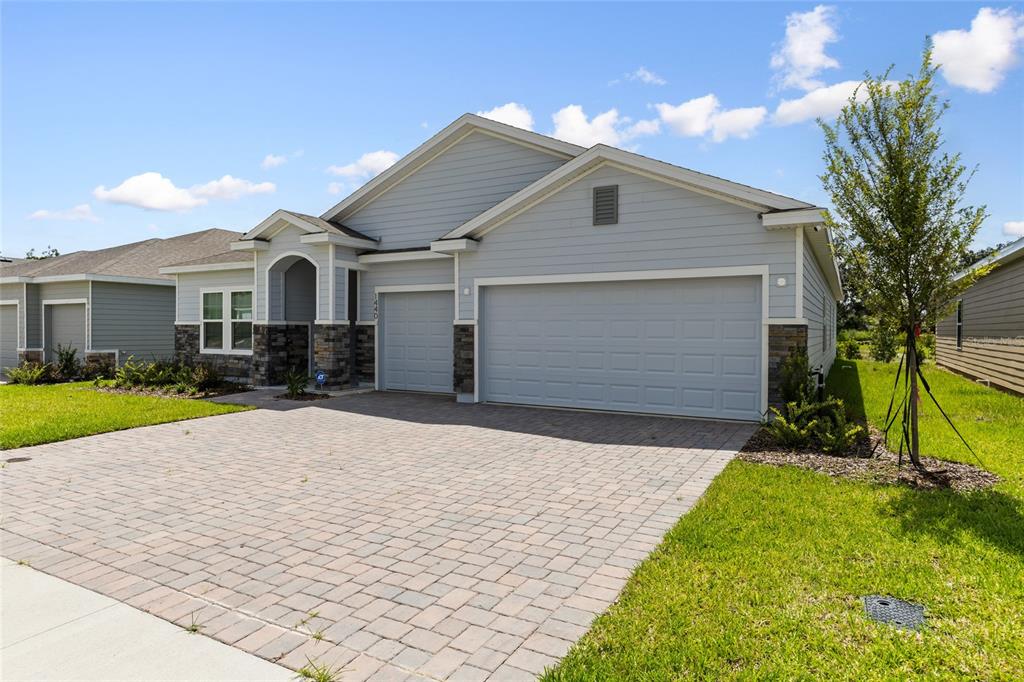 A light blue house with a stone-accented facade and a paved driveway under a blue sky — 1440 NW 128 TERRACE, NEWBERRY, FL