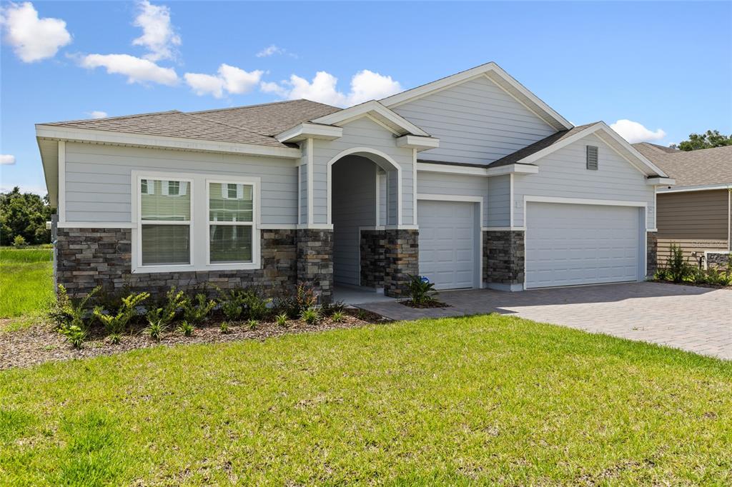 A light blue house with stone veneer accents, a three-car garage, and a paved driveway — 1440 NW 128 TERRACE, NEWBERRY, FL