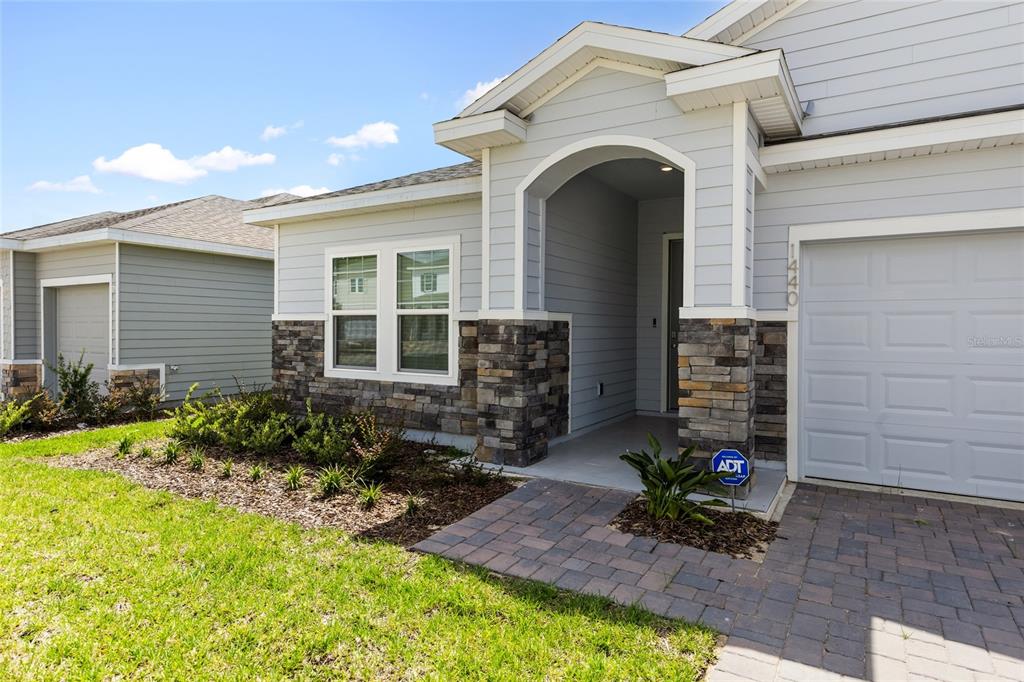 A single-story house exterior features light gray siding, stone accents, and a paved walkway — 1440 NW 128 TERRACE, NEWBERRY, FL