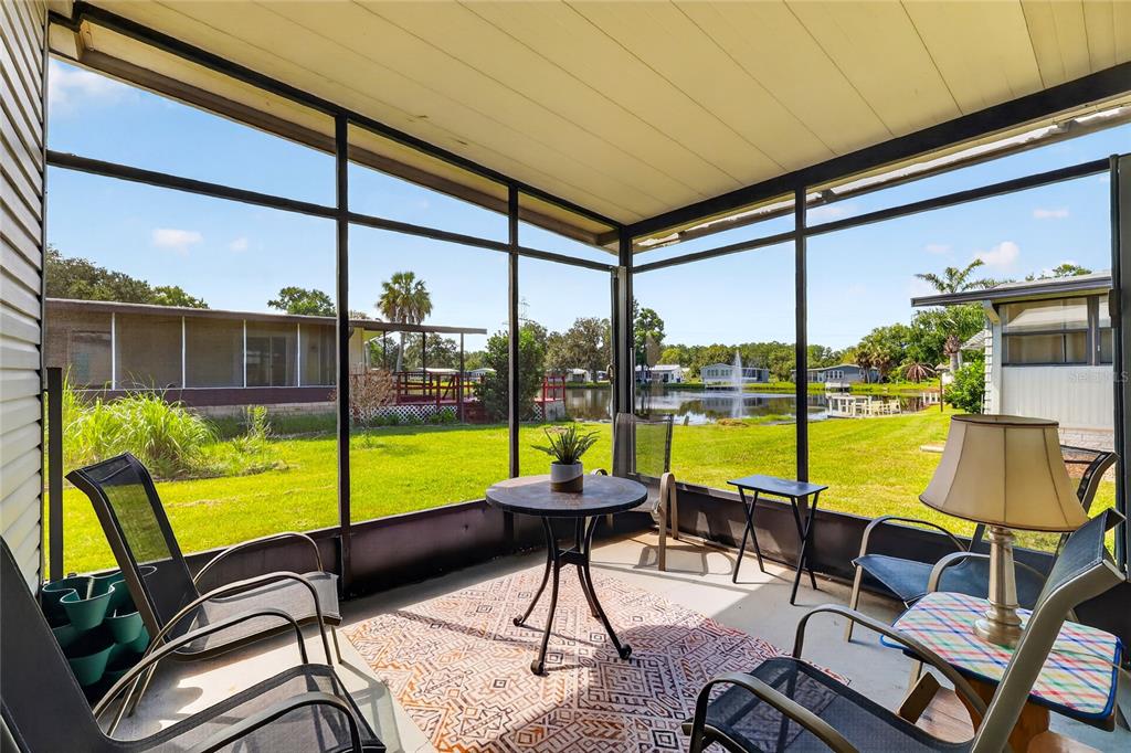 A screened-in porch with outdoor furniture overlooks a grassy yard and a small pond — 12 N BOBWHITE ROAD, WILDWOOD, FL