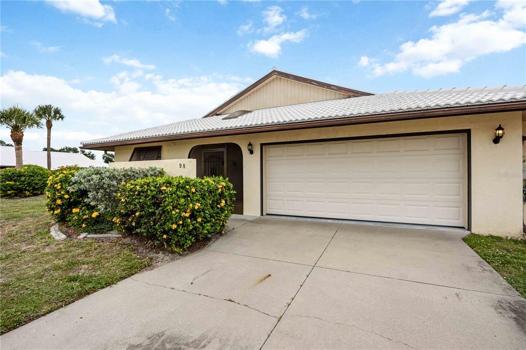 A single-story house with a white garage door, a tiled roof, and a landscaped front yard — 98 DRIFTING SANDS DRIVE, VENICE, FL