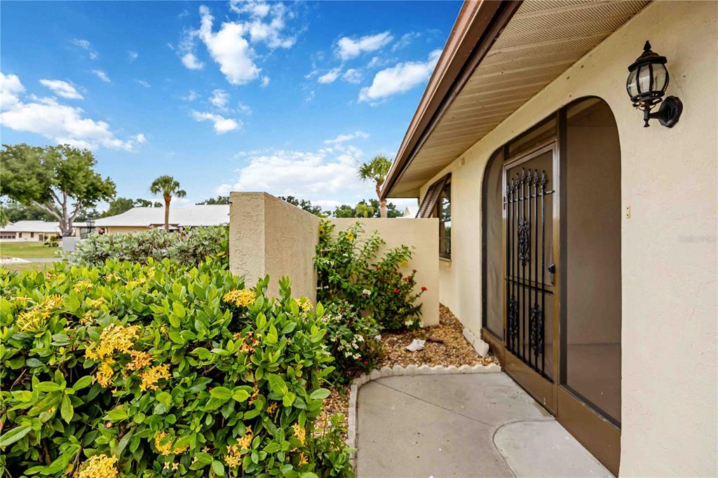 A concrete walkway leads to a front door with a decorative black metal security screen — 98 DRIFTING SANDS DRIVE, VENICE, FL