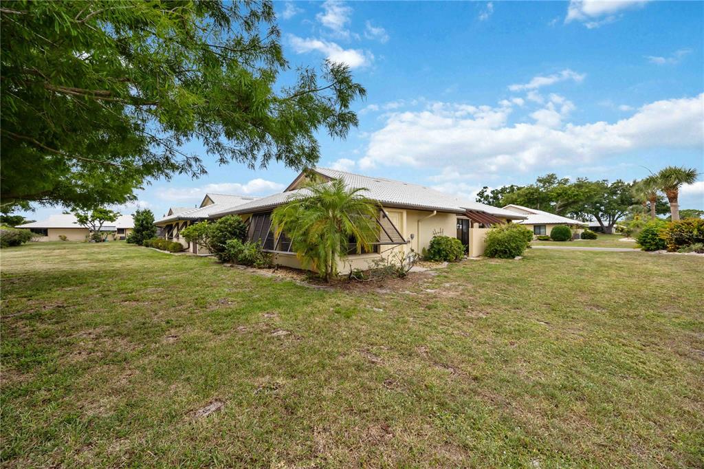 A low-slung, light-colored residential building sits on a grassy lawn under a blue sky — 98 DRIFTING SANDS DRIVE, VENICE, FL