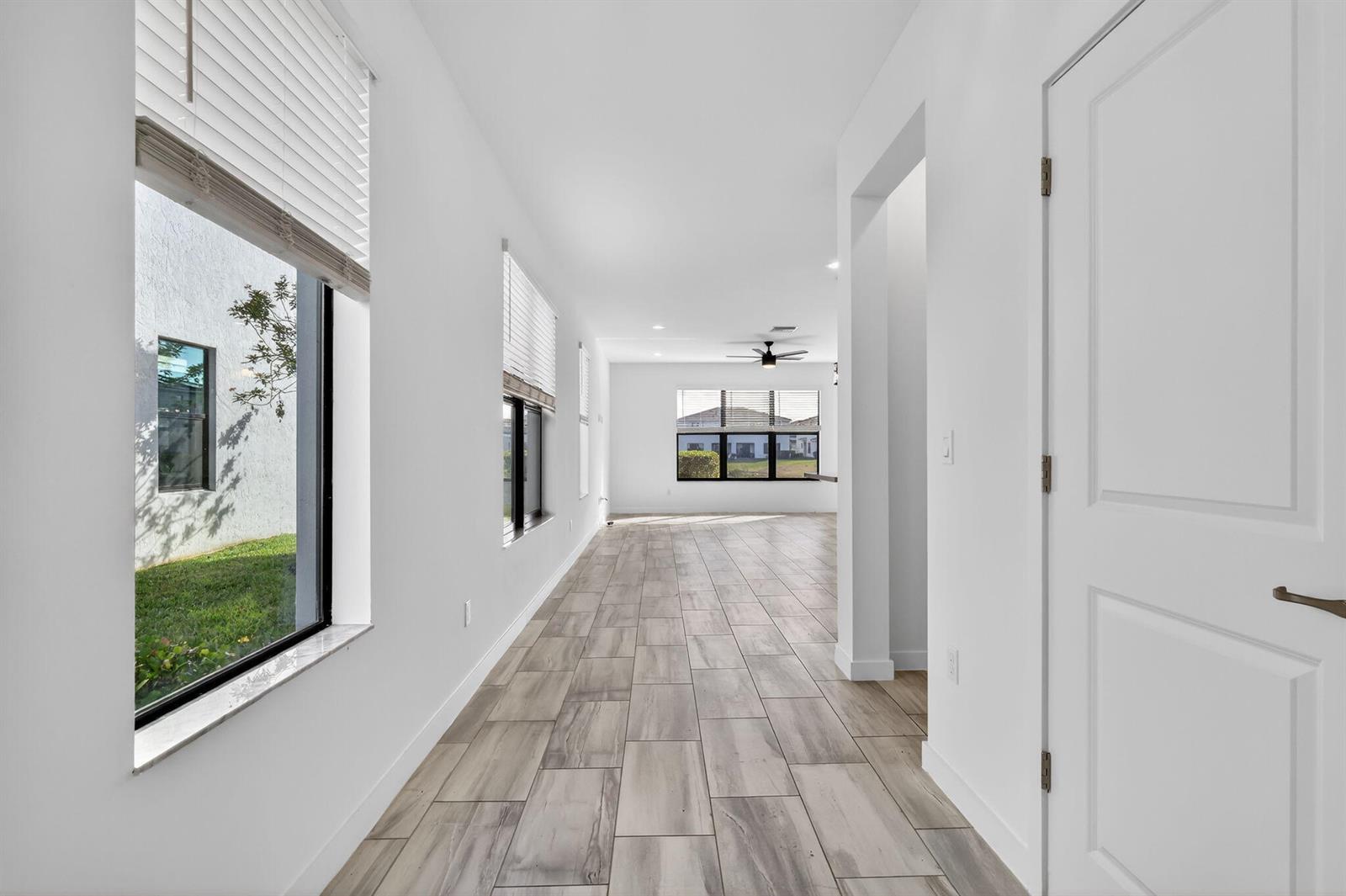 A bright hallway with light wood-look tile flooring leads toward an open living area — 8792 Antarus Drive, Lake Worth FL 33467, LAKE WORTH, FL