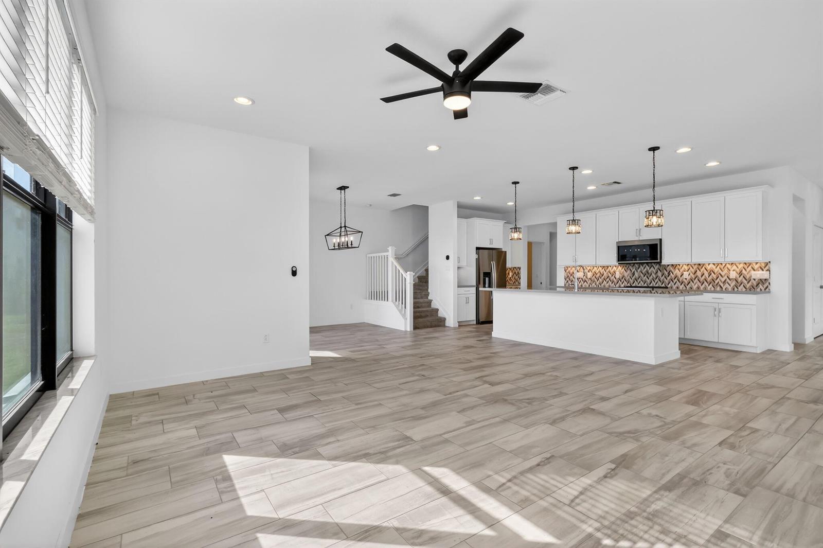 A bright, open-concept kitchen and living area featuring white cabinetry, wood-look tile floors, and stairs — 8792 Antarus Drive, Lake Worth FL 33467, LAKE WORTH, FL