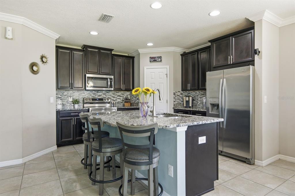 A kitchen features dark wood cabinets, granite countertops, a central island, and stainless steel appliances — 18793 DEER TRACKS LOOP, LUTZ, FL