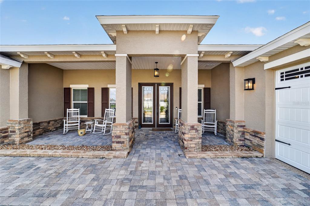 A paved driveway leads to a covered front porch with rocking chairs and stone columns — 8370 SW 99TH TERRACE, OCALA, FL