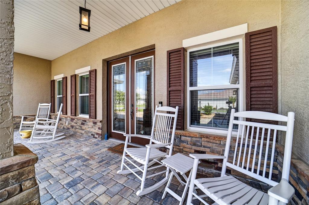 A covered front porch features stone siding, paver flooring, and four white rocking chairs — 8370 SW 99TH TERRACE, OCALA, FL
