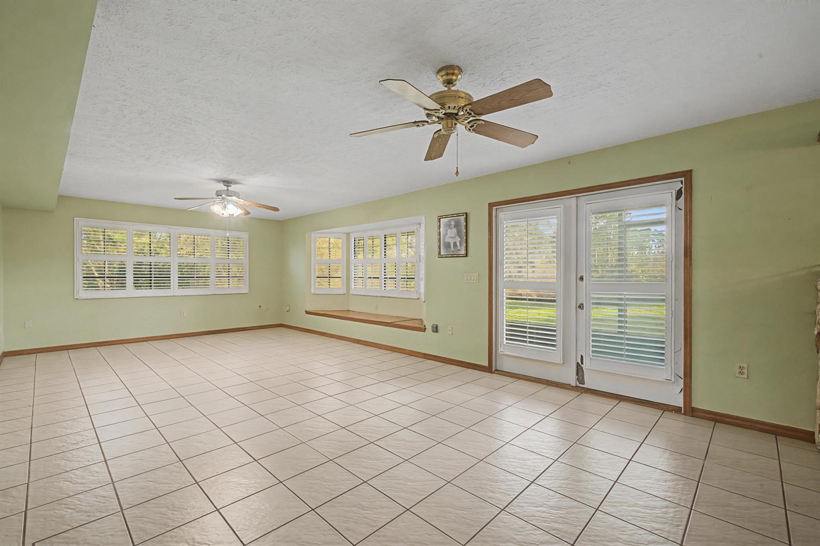 A spacious room with light green walls, tiled floors, two ceiling fans, and a bay window — 665 Moon Ranch Road, Sebring FL 33870, SEBRING, FL