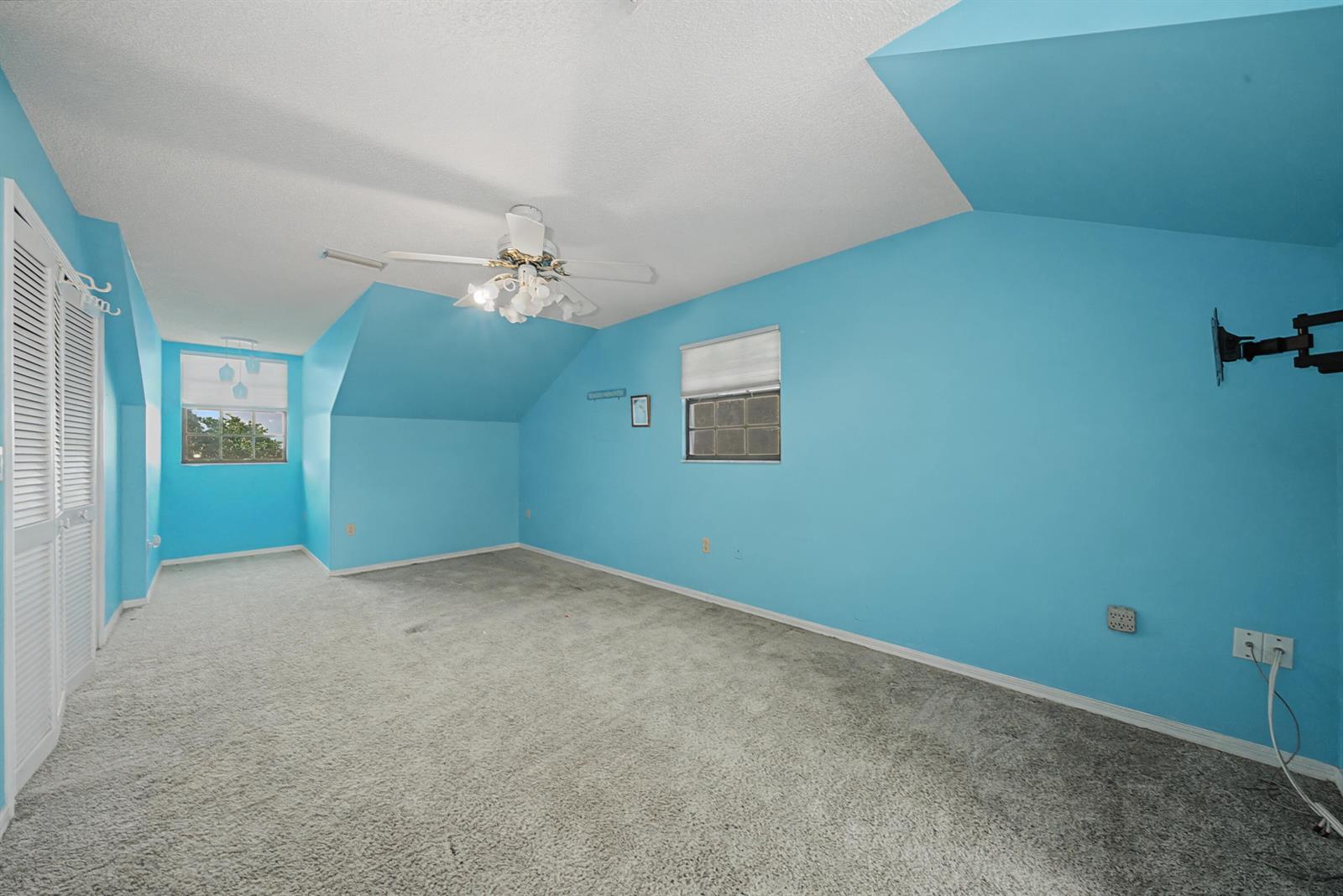 An empty bedroom with bright blue walls, gray carpeting, a ceiling fan, and sloped ceilings — 665 Moon Ranch Road, Sebring FL 33870, SEBRING, FL