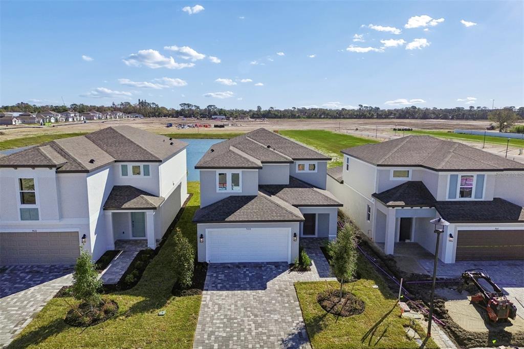 An aerial view shows three modern two-story houses with paved driveways and a nearby pond — 9018 OPTIMIST WAY, PALMETTO, FL