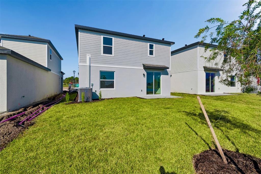 The rear exterior of a two-story house features gray siding, a small patio, and lawn — 9018 OPTIMIST WAY, PALMETTO, FL
