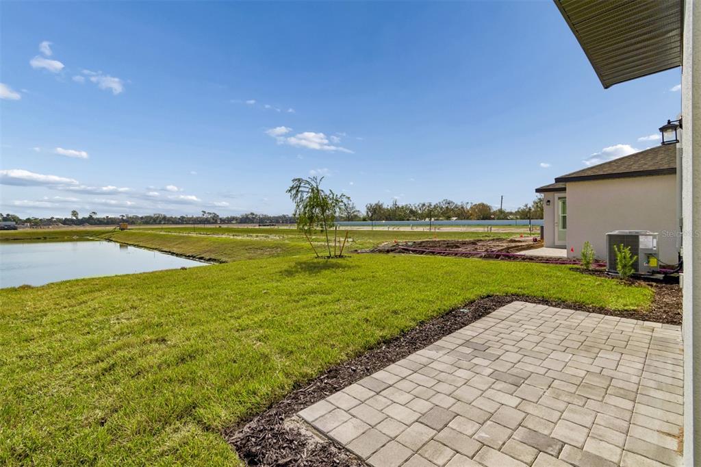 A paved patio overlooks a grassy yard, a small pond, and a neighboring house — 9018 OPTIMIST WAY, PALMETTO, FL